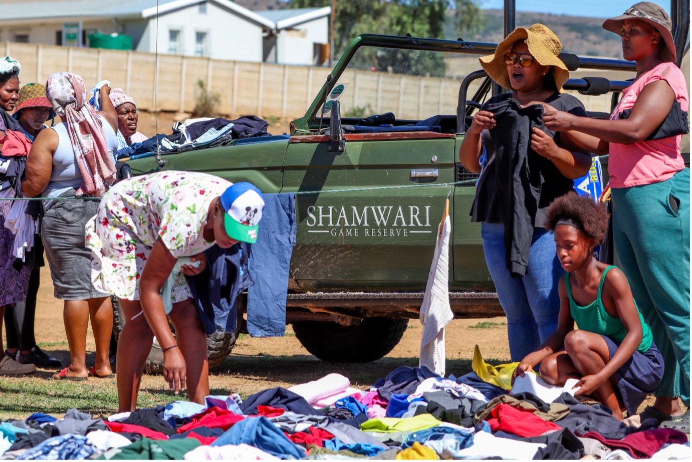 The Alicedale community members surround the piles of clothing, sifting through them to find items for themselves and/or their loved ones. On the far left, the four women there are putting aside all the clothes they want on the bonnet of the Shamwari vehicle. Occasionally, having playful arguments over clothing items. Photo: Abigail Van der Hoven